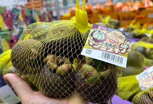 黄色いネットに沢山入ったコストコ マンゴスチンをつかんでいる手 551130
