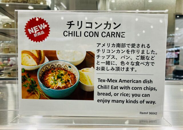 コストコ倉庫店の紹介チラシ。チリコンカン新発売を告知する黒地に赤いスパイス風デザイン。商品写真、商品名『CHILI CON CARNE』、ITEM#96042、新商品タグ、具材（牛肉・豆・トマト）の説明、盛り付けイメージと“ごはん・パン・タコスにおすすめ”のキャッチコピーが入った販促ポスター風デザイン