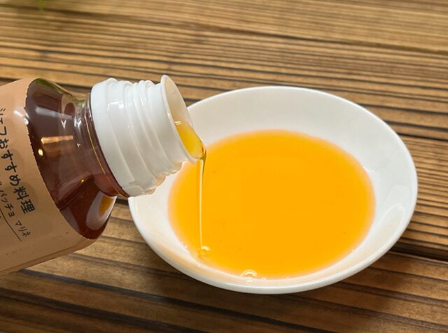 ピエトロ ガーリックオイルを白い皿に注いでいる様子。透明感のある茶褐色のオイルが特徴的