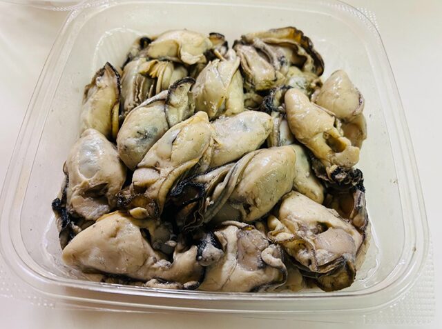 コストコの焼き牡蠣（ITEM#94395）を透明な正方形ポリパックから開封した様子。殻なしで調理済みの牡蠣がたっぷり入った冷蔵デリ商品
