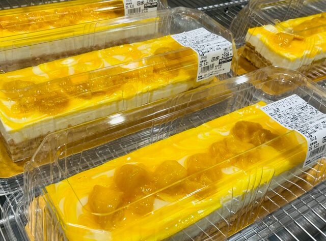夏らしい店頭に並ぶマンゴークランチーヨーグルトケーキ。サクサクのアーモンドスポンジにマンゴーとヨーグルトクリームが層になったケーキが、透明ケースに入って棚に整列している様子