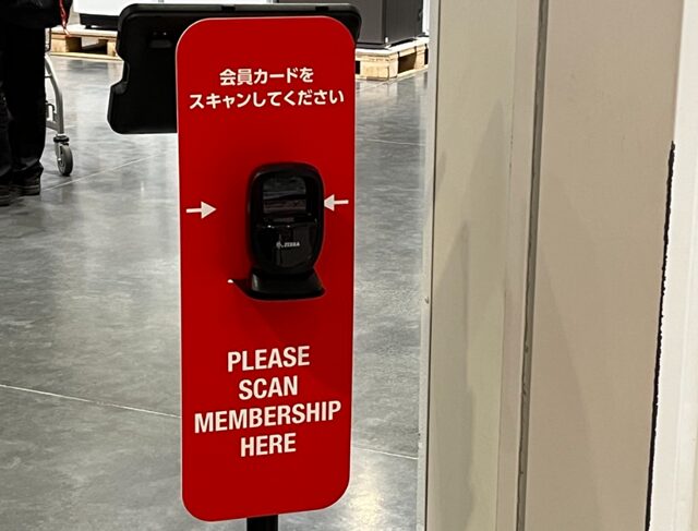 コストコのスタンド型バーコード入店チェック機械。表面に『会員カードをスキャンしてください』と表示されている画面