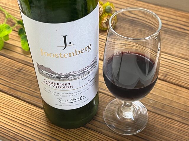 コストコ「ユステンバーグ カベルネ・ソーヴィニヨン」ITEM#518726。赤ワインをグラスに注いだシーンとボトルの写真。深みのあるルビーレッドの色合いと芳醇なカシスやプラムの香りが漂う、南アフリカ・ステレンボッシュ産のフルボディワイン。