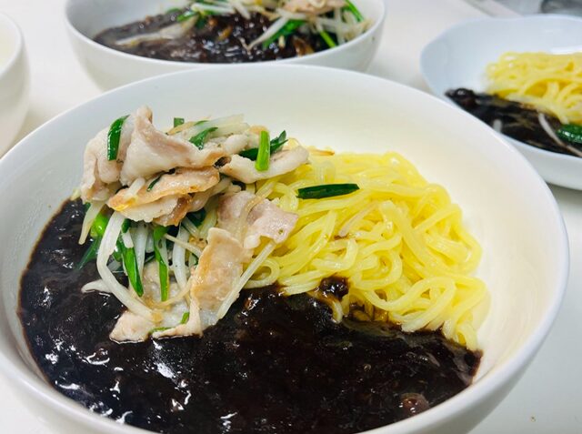 調理した韓国ジャージャー麺を皿に盛りつけ、ニラ・もやし・バラ肉の炒め物をトッピングした完成写真。